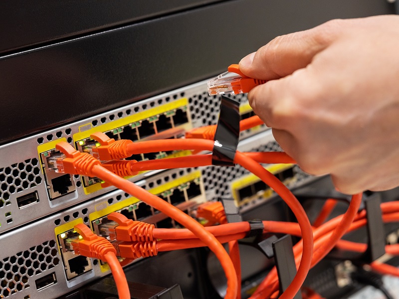 Cropped hand of male IT engineer plugging network cable in router cluster at datacenter
